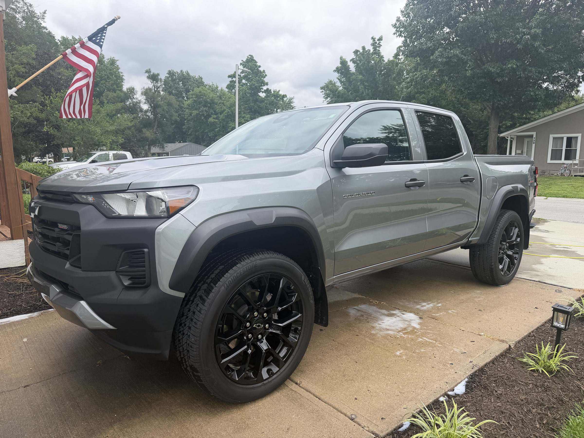 Silver Chevrolet Colorado pickup on a driveway with an American flag in the background